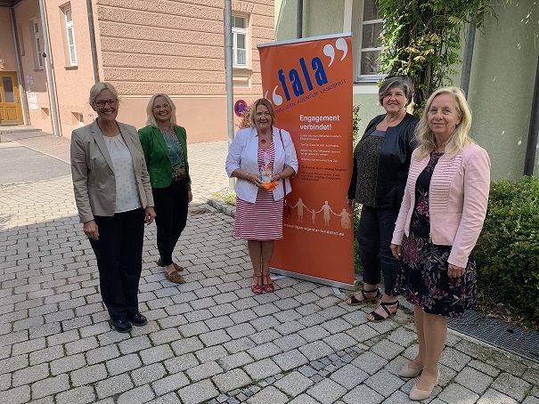 Fünf Frauen vor einem Werbeständer im Außenbereich, fröhliche Gesichter