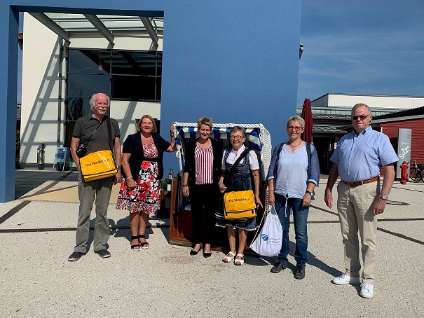 Menschen mit gelben Taschen stehen vor blauer Mauer