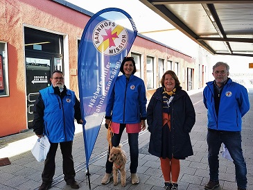 Vier Menschen mit der Flagge der Bahnhofsmission