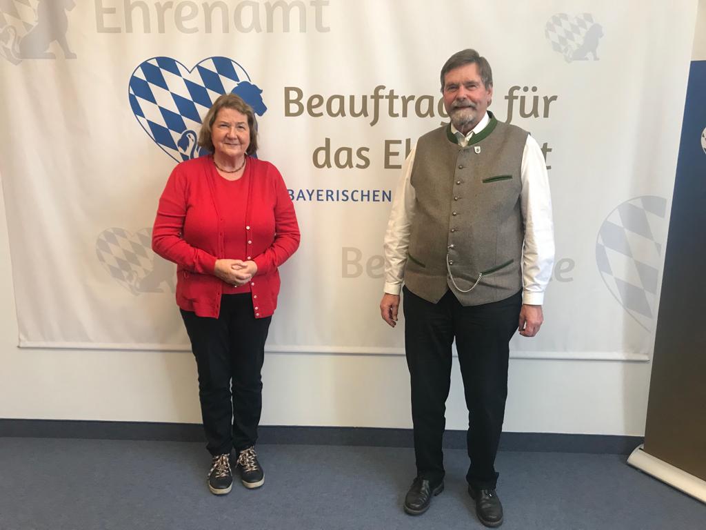 Mann und Frau vor einer Wand mit Logo der Ehrenamtsbeauftragten