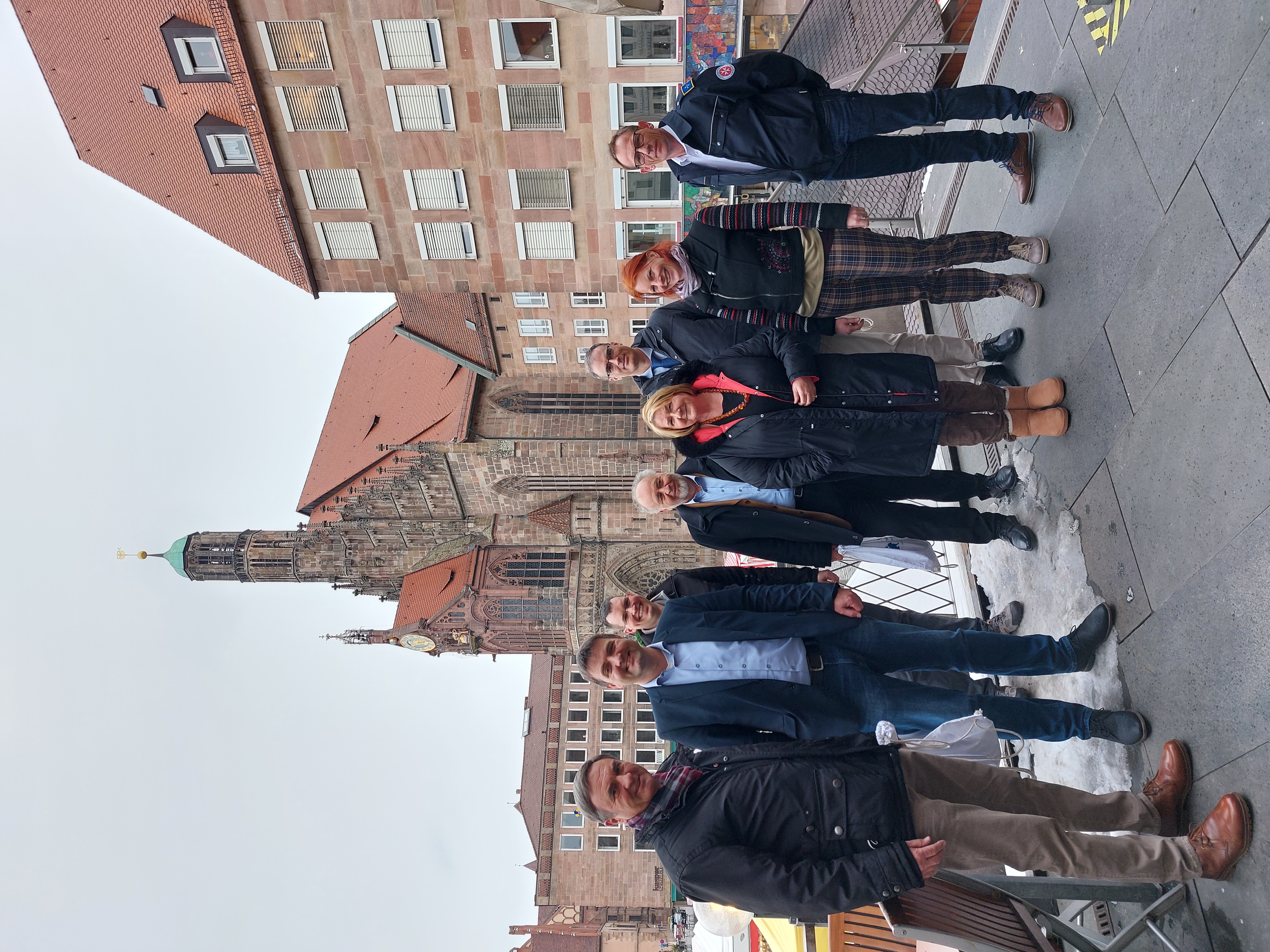 8 Personen, auf einer Terrasse, im Hintergrund eine große Kirche