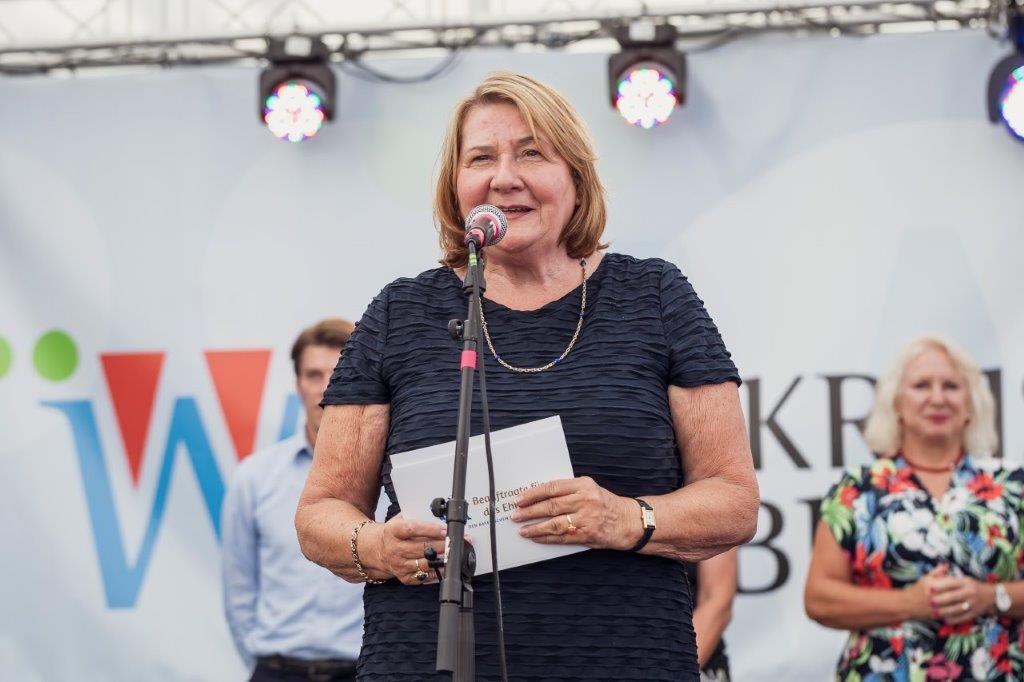 Eine Person an einem Mikrofon, stehend, sprechend, hält Karten in der Hand