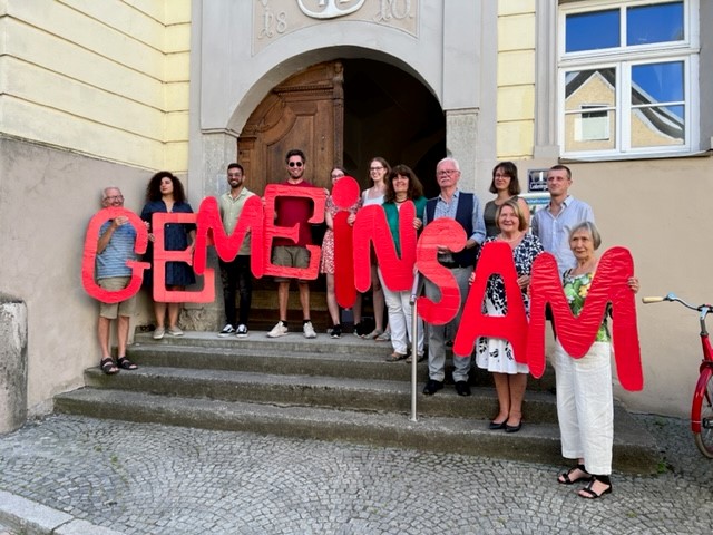 viele Menschen halten einen Buchstaben hoch und bilden das Wort gemeinsam