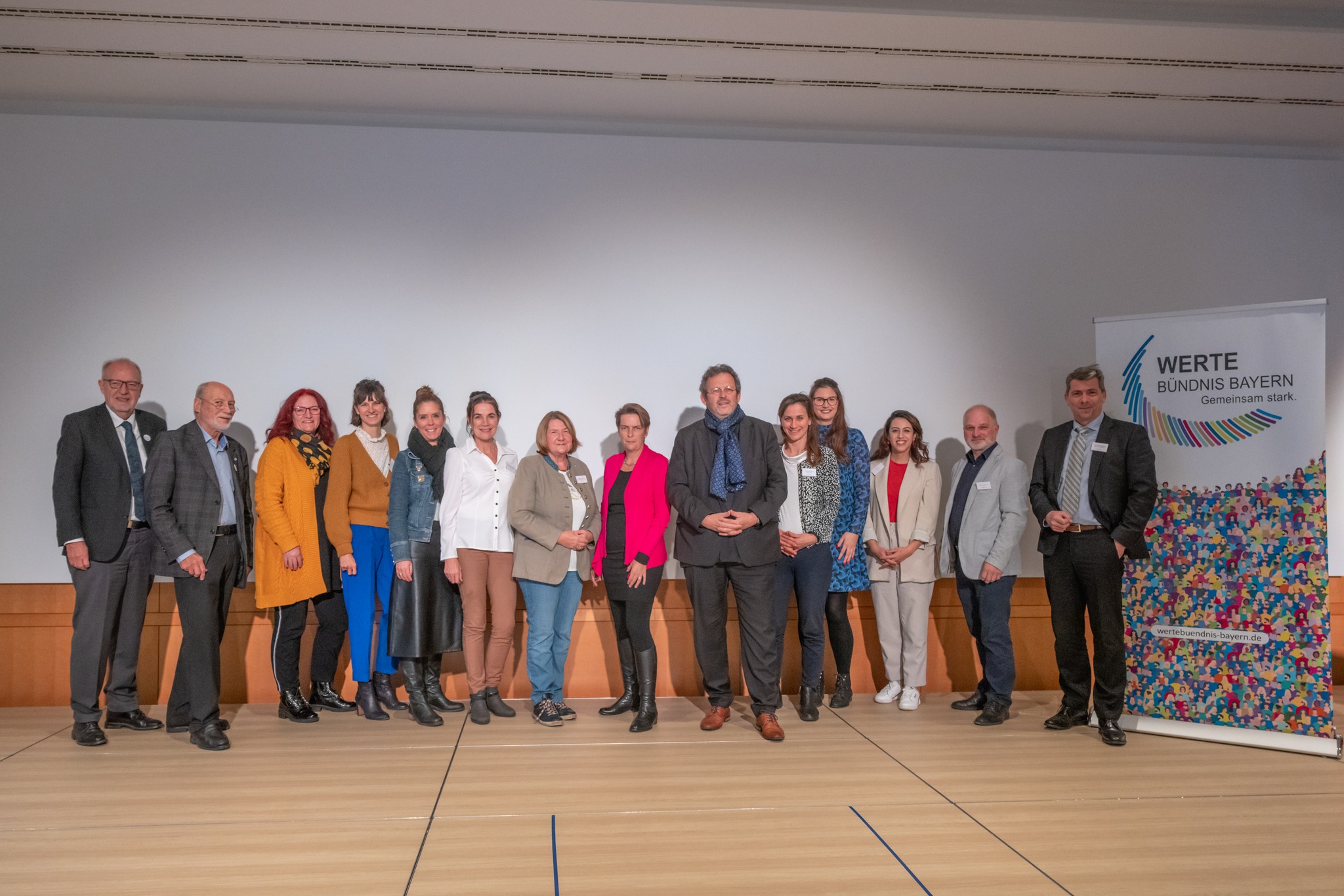 Vierzehn Personen stehen vor einer weißen Wand und werden fotografiert