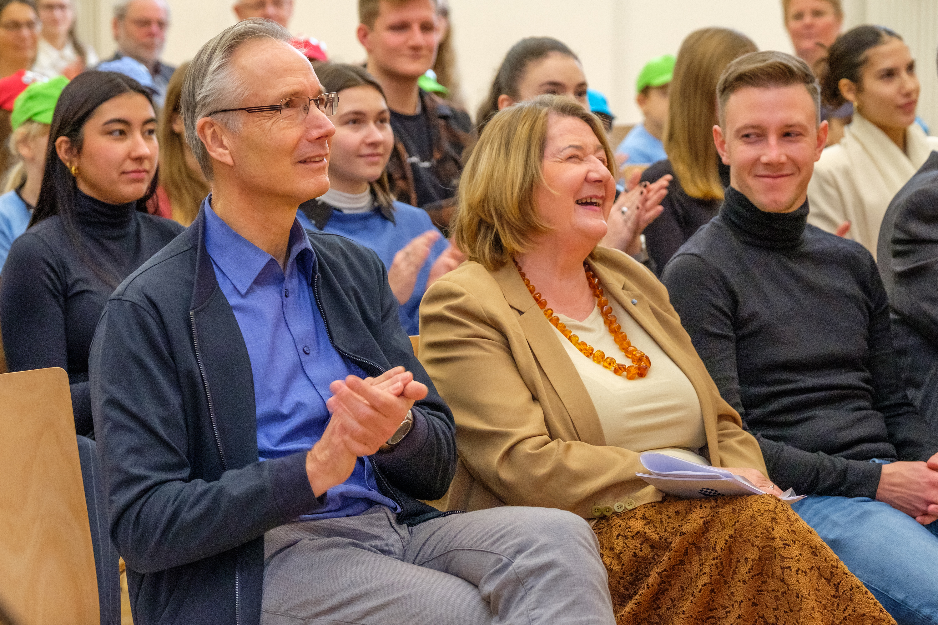 Mehrere Menschen sitzen auf Stühlen im Publikum und lachen, sind glücklich