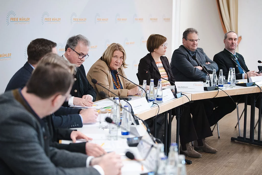 Acht Personen sitzen an einem Konferenztisch und reden miteinander