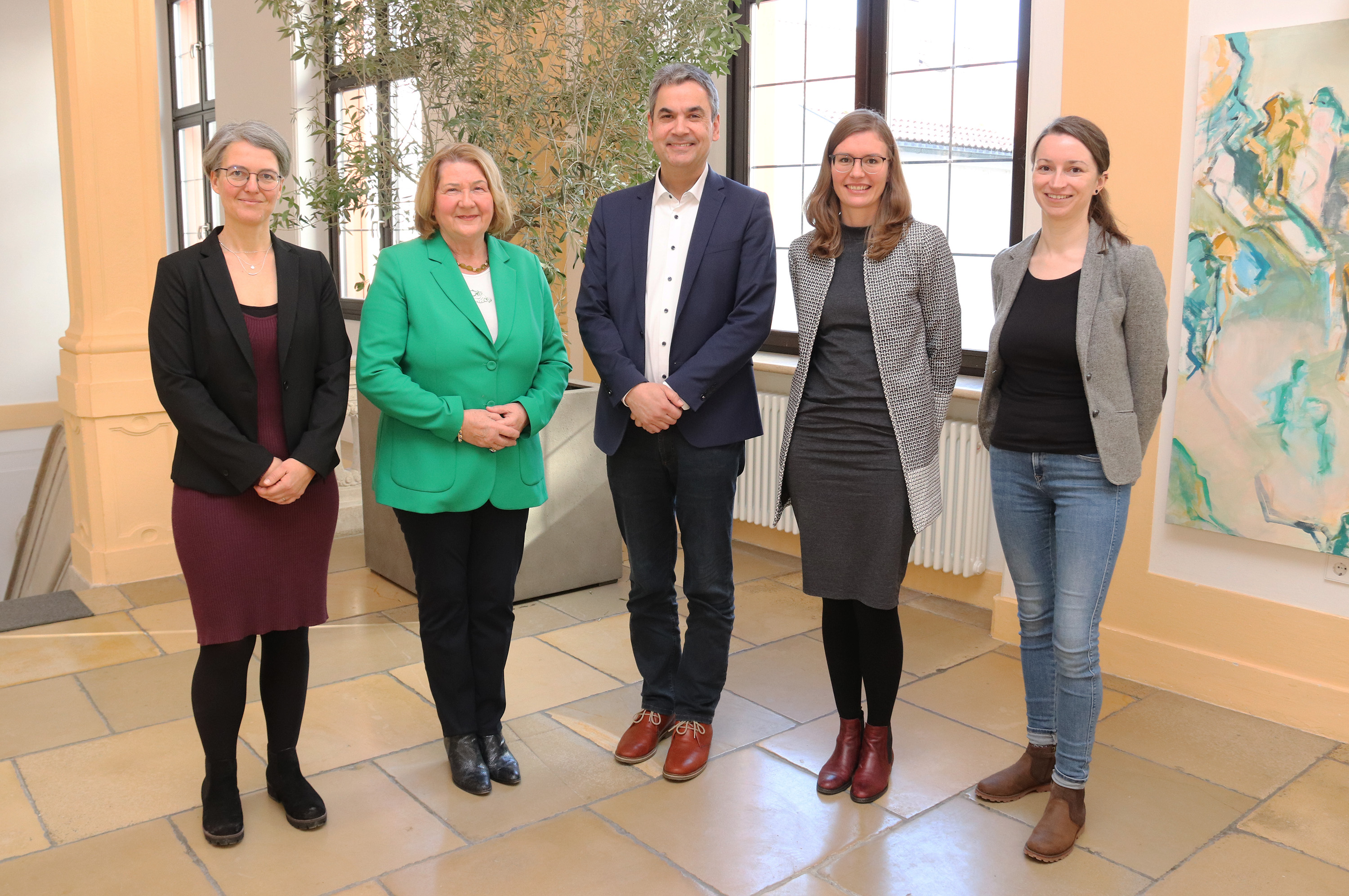 Fünf Personen in einer Reihe darunter ein Mann in der Mitte, alle lächeln in Richtung einer Kamera