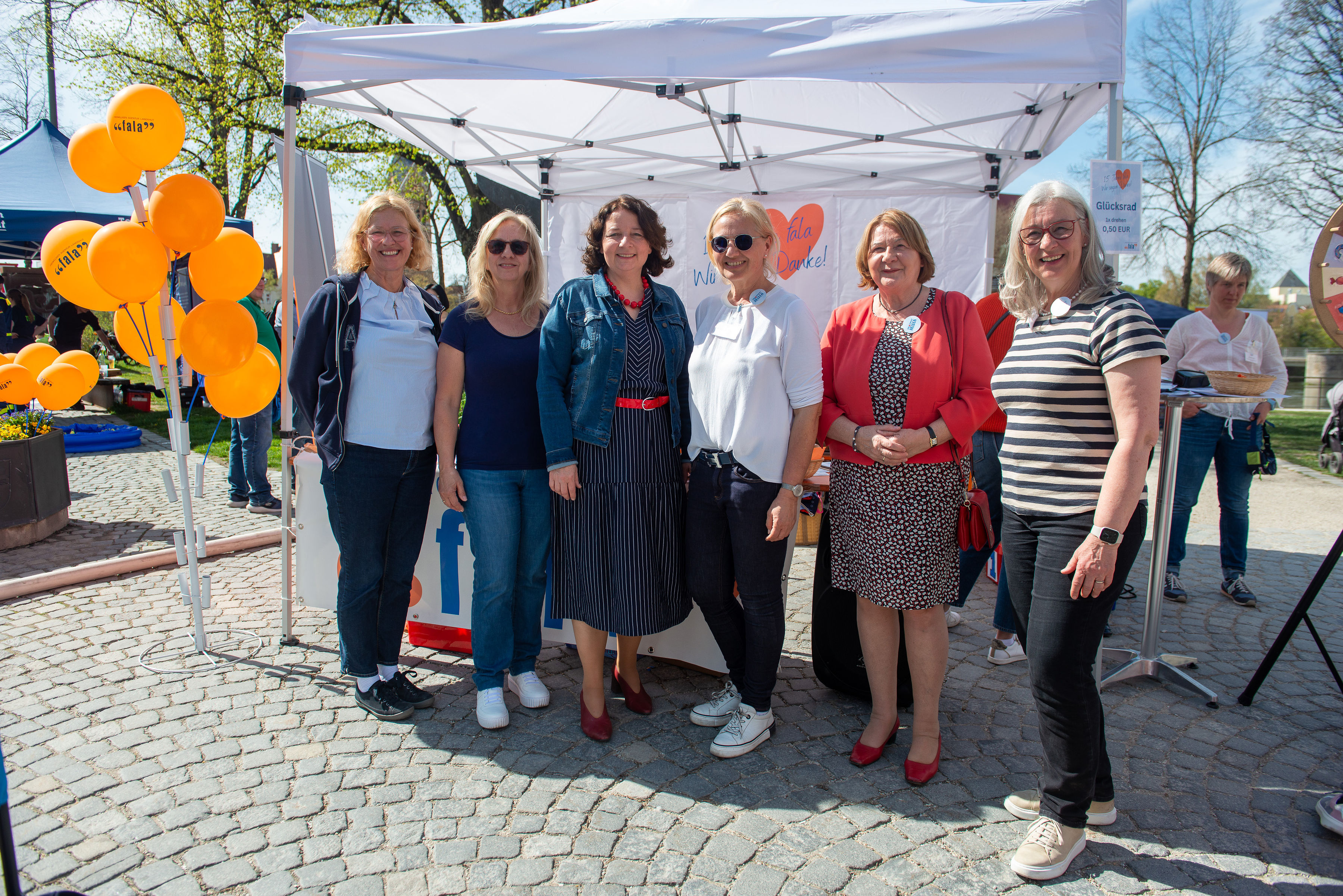 Sechs Personen stehen vor einem Pavillon bei sonnigem Wetter