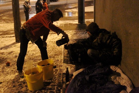 Ein Mann schenkt einem Obdachlosen ein Getränk aus einer Thermoskanne
